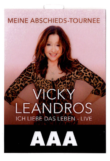 Portrait of Vicky Leandros smiling with hands on hips, wearing a leopard print top, promoting her farewell tour 'Ich liebe das Leben - Live'.